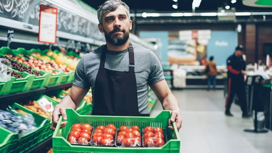 Un trabajador de una tienda de abarrotes sostiene una caja de jitomates