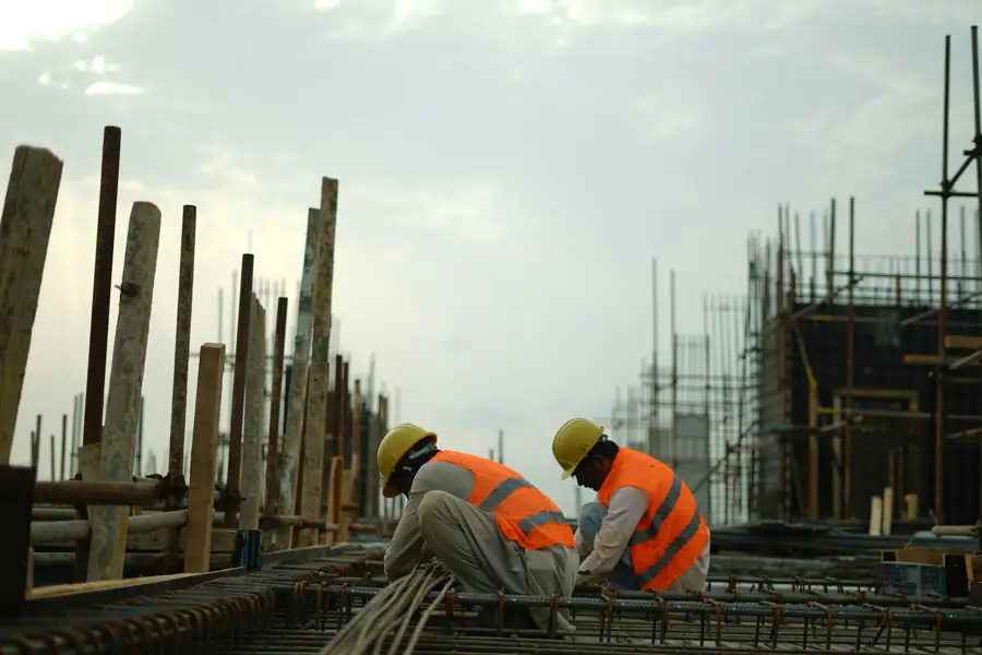 Dos trabajadores con casco arman varilla en una obra al atardecer