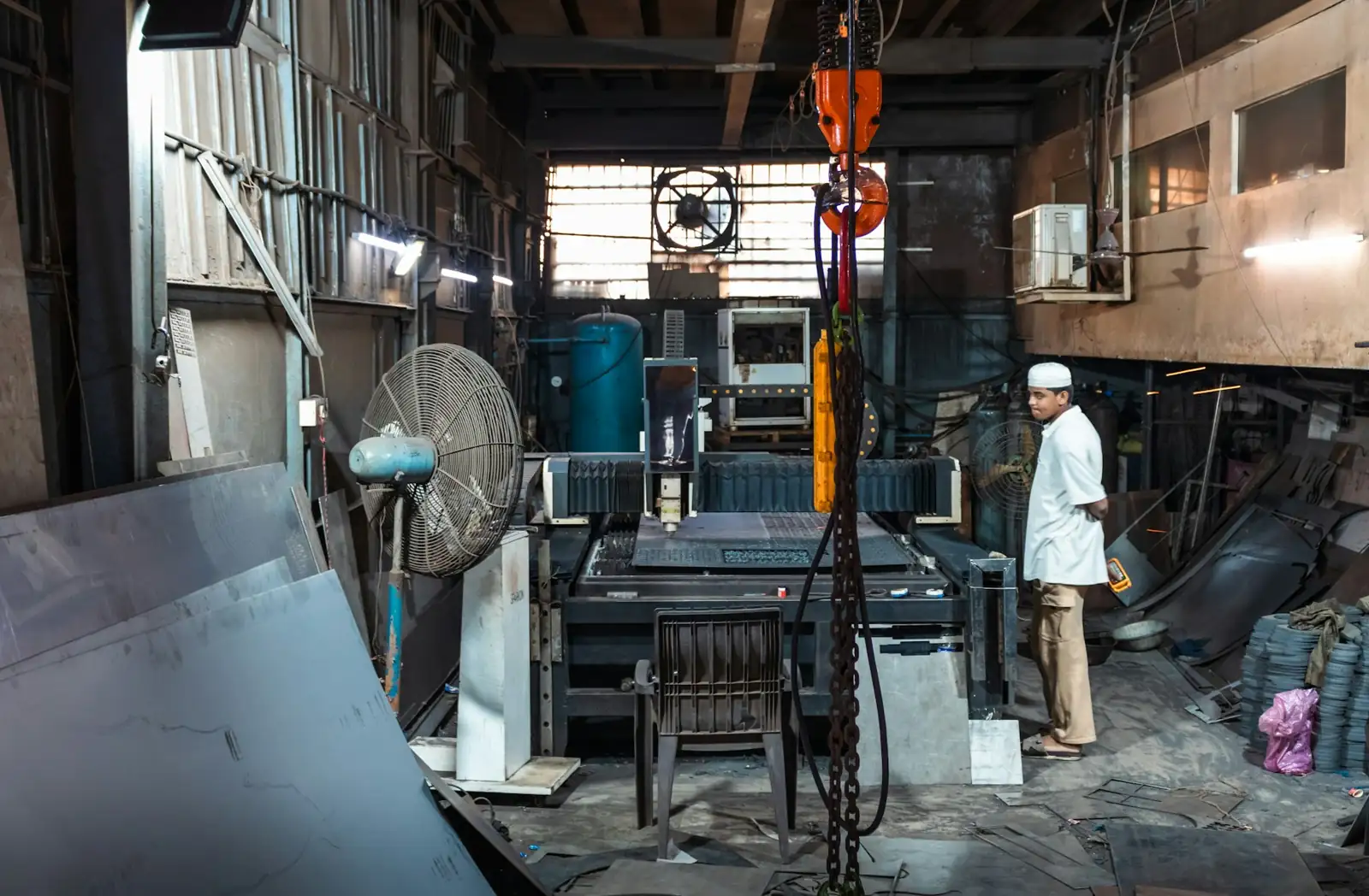 Un hombre de pie dentro de un taller industrial lleno de material y maquinaria