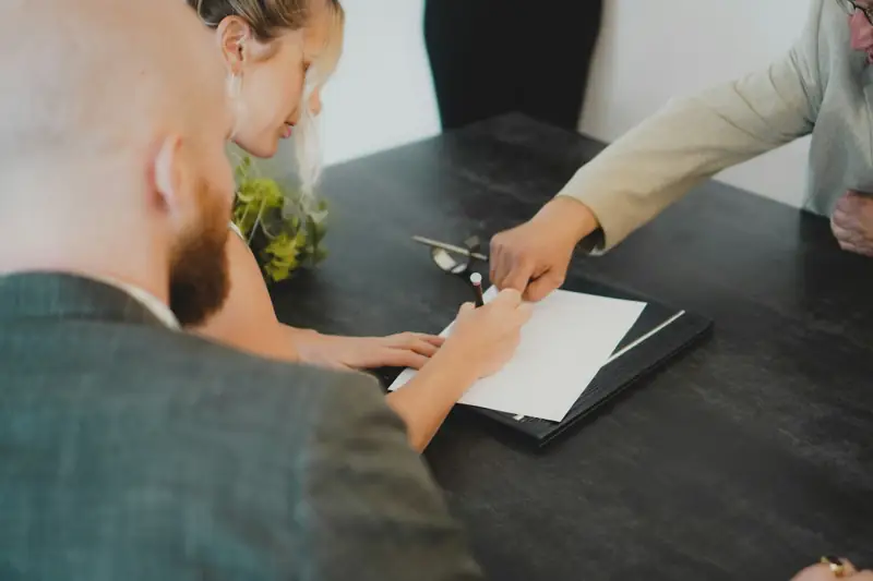 Dos personas firman un contrato frente a un asesor en un escritorio