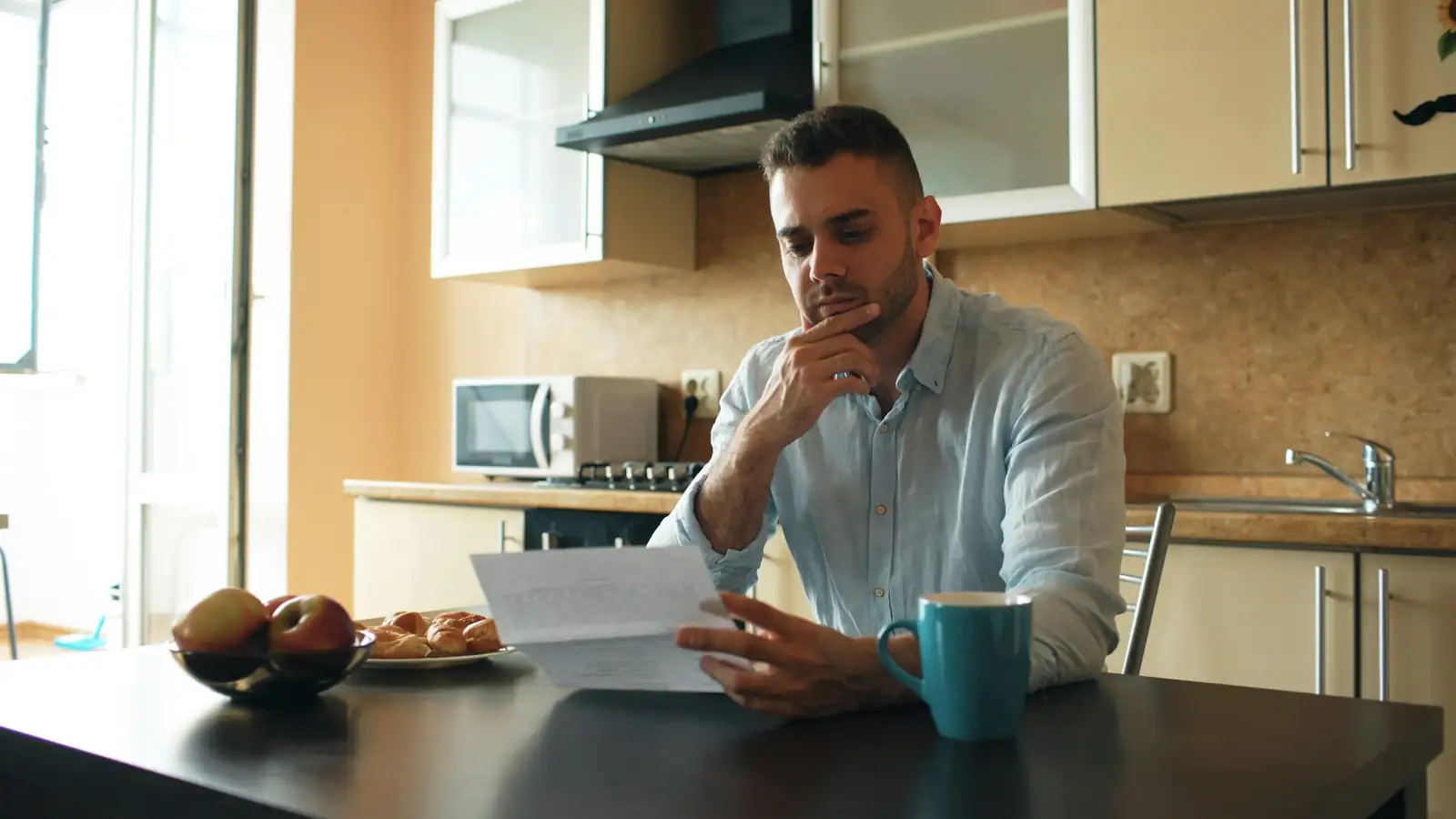 Un hombre revisa con preocupación un recibo en la mesa de su cocina